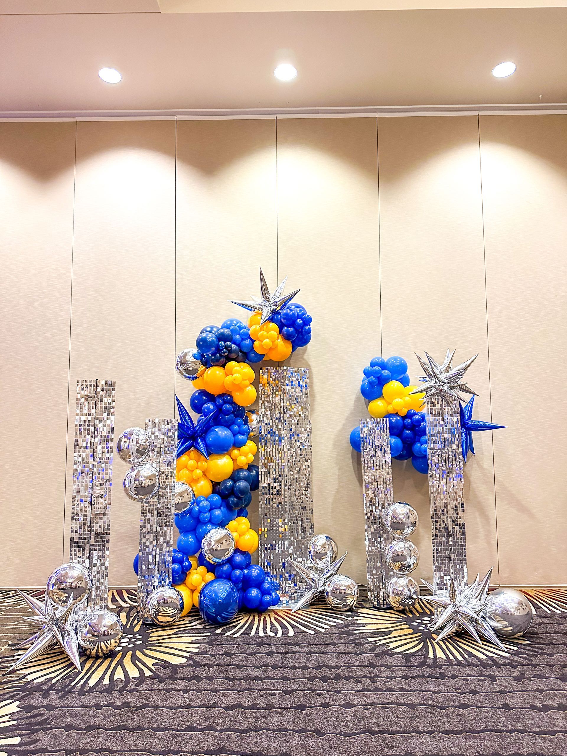 Balloon display with blue, yellow, and silver elements against a patterned backdrop.