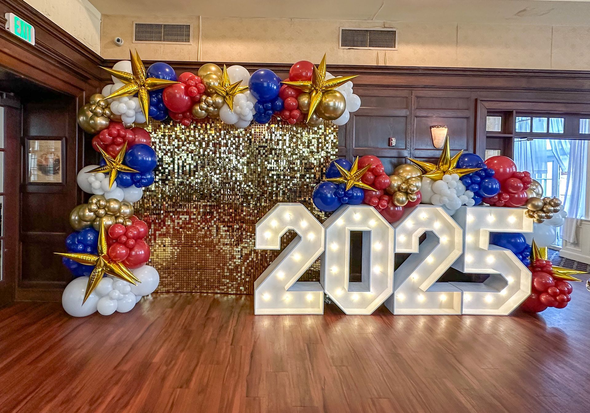 Balloon arch with star and number 2025 decorations for a celebration; gold, red, blue, and white.