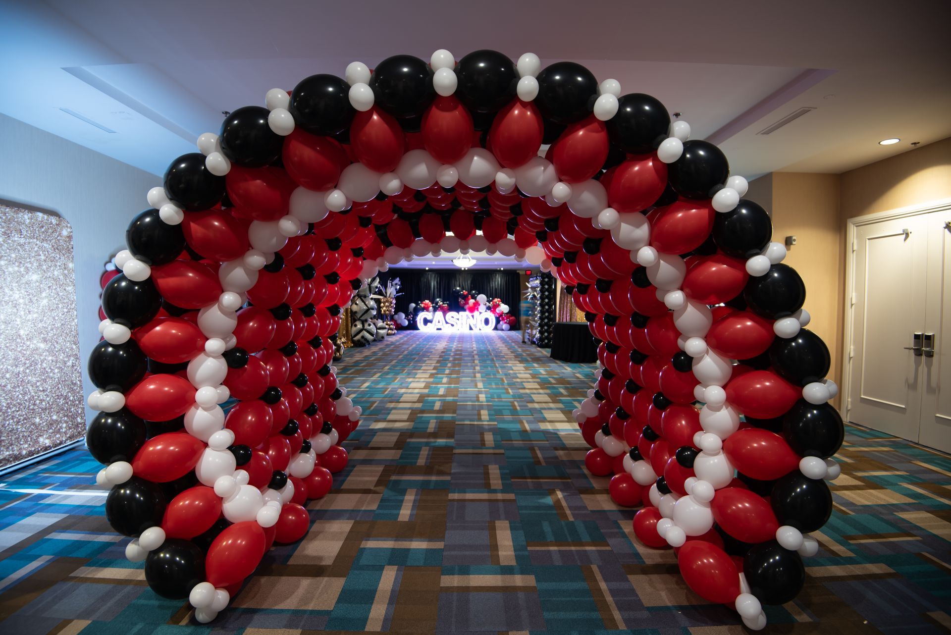 Balloon archway in red, black, and white over a hallway with patterned carpet.