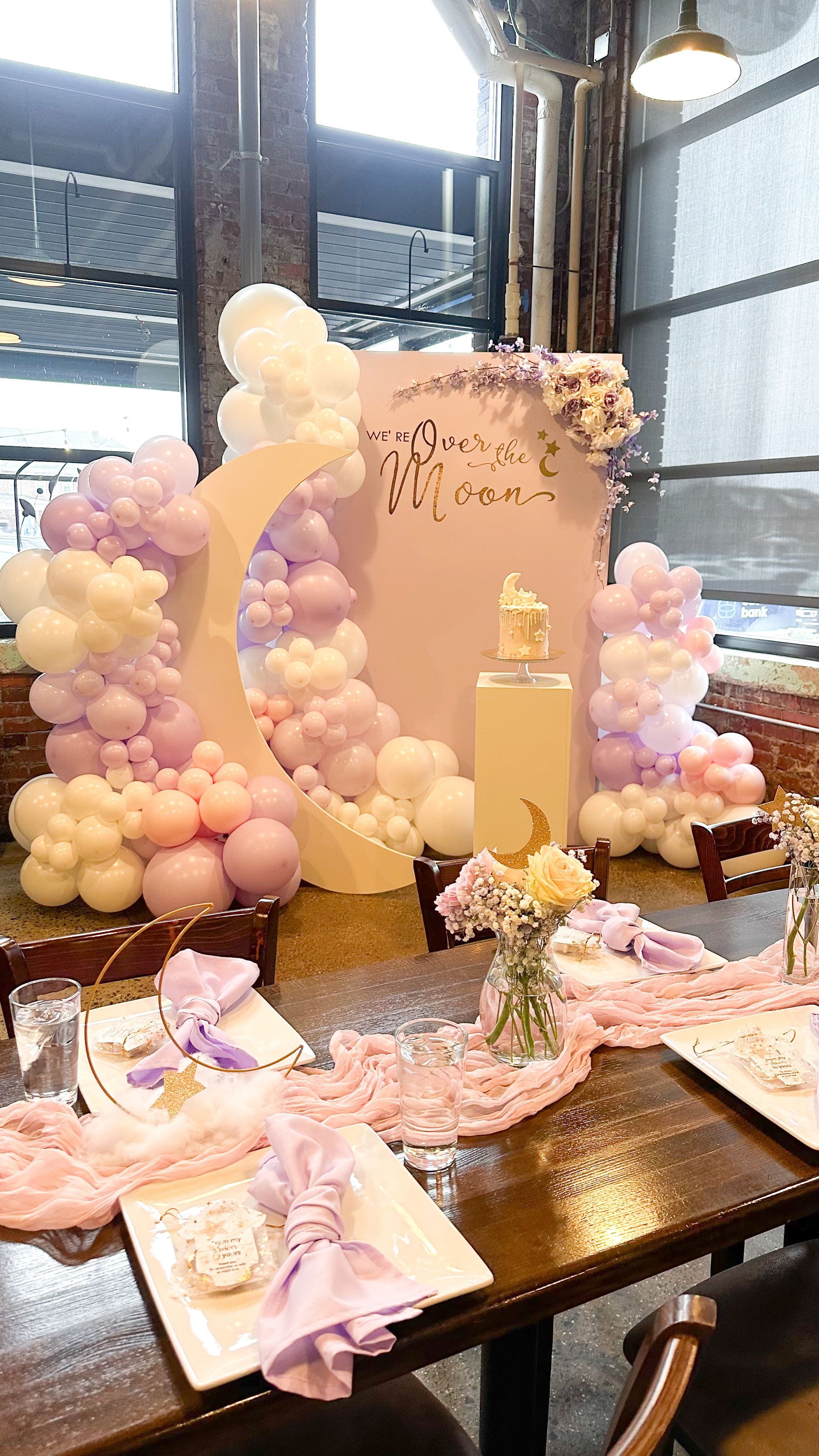 Birthday party table with lavender and cream balloons, a moon backdrop, and a cake.