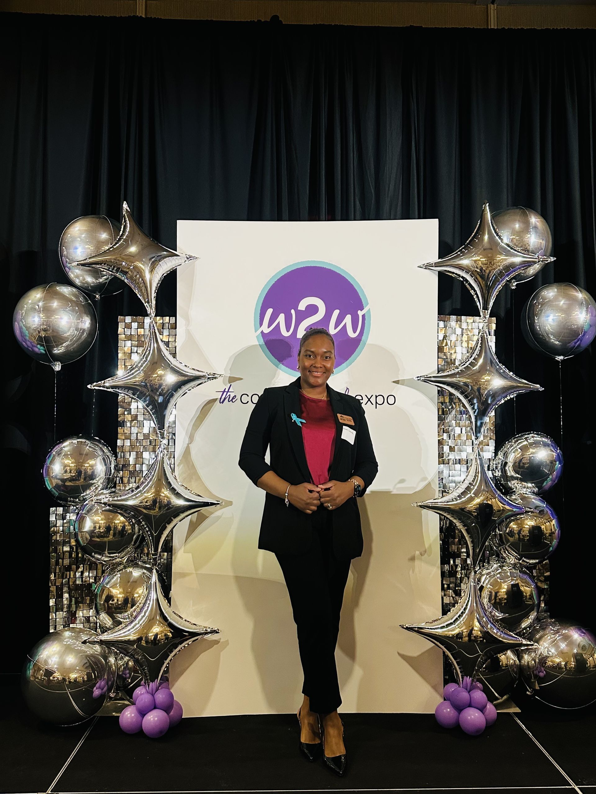 Woman in suit poses in front of a backdrop with balloons.