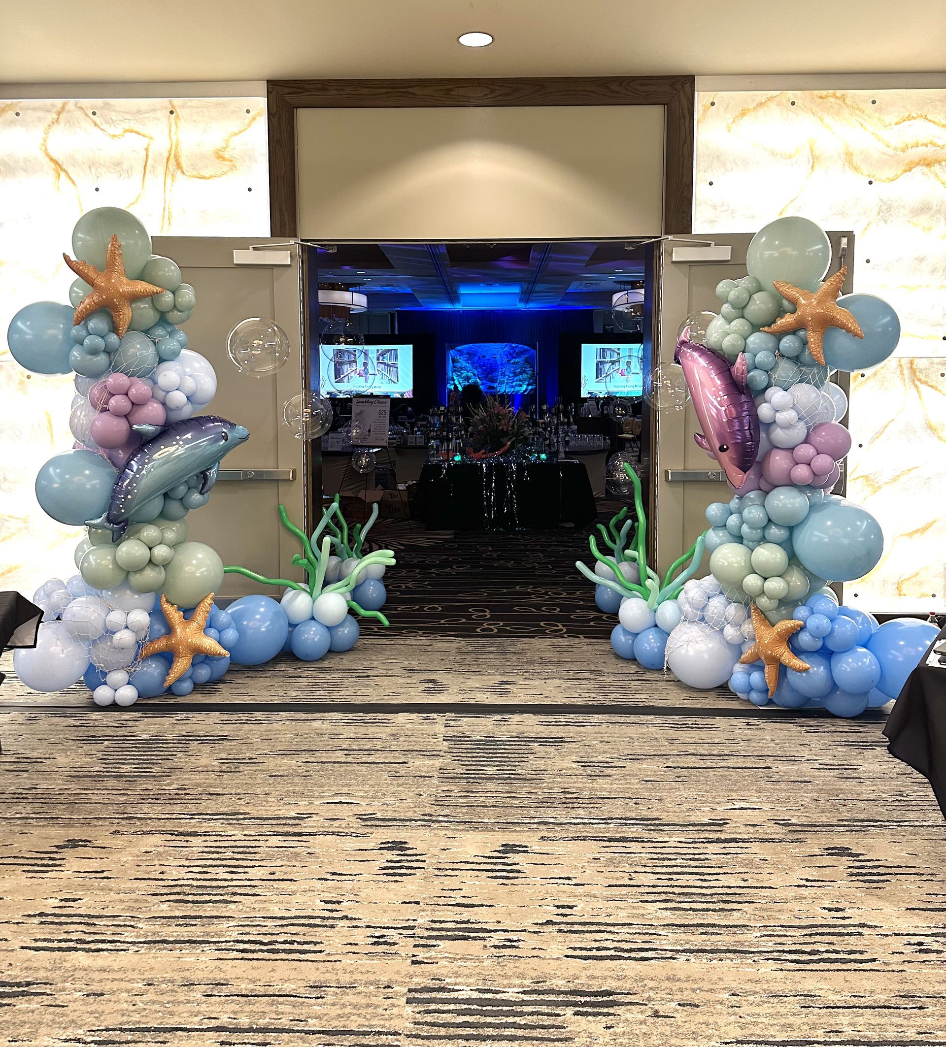 An under-the-sea themed balloon archway at an event entrance, featuring various shades of blue, green, and pink balloons.