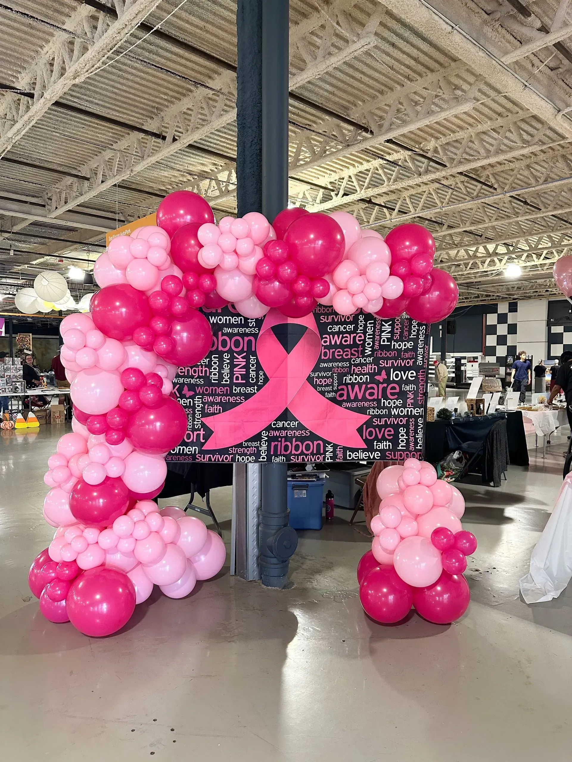 Pink balloon arch with breast cancer awareness sign and ribbon.