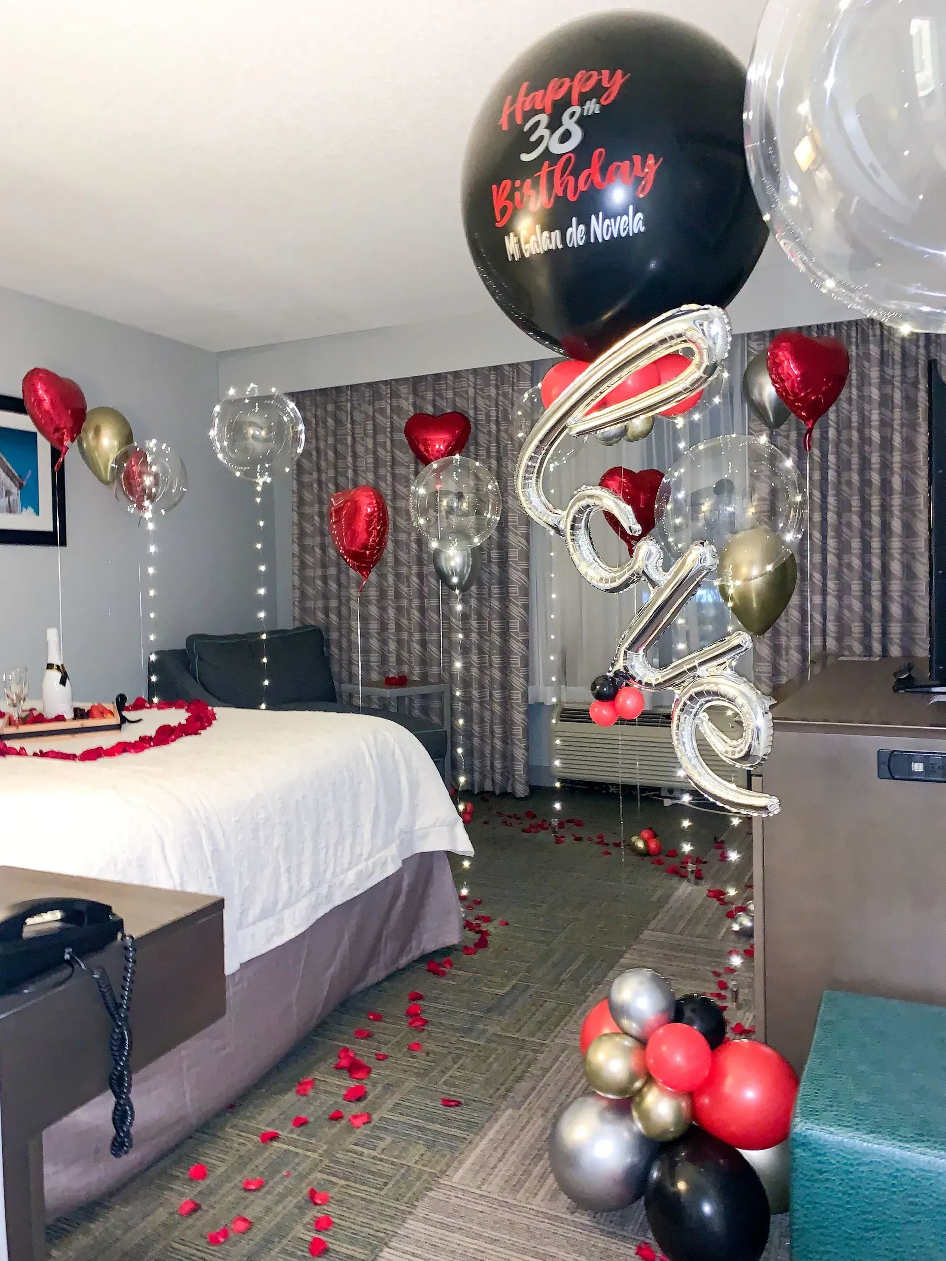 Hotel room decorated with balloons and rose petals for a birthday celebration.