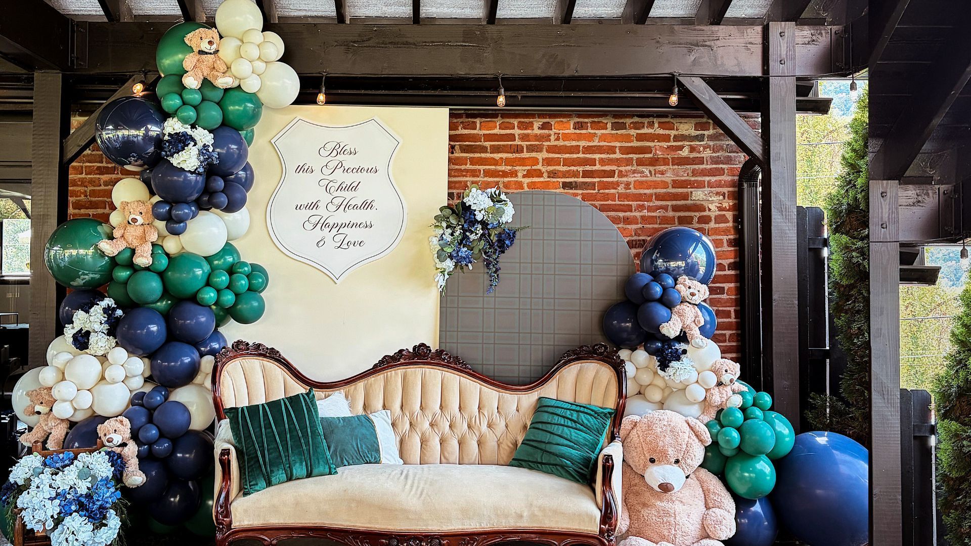 Balloon arch backdrop with a beige sofa and teddy bears.