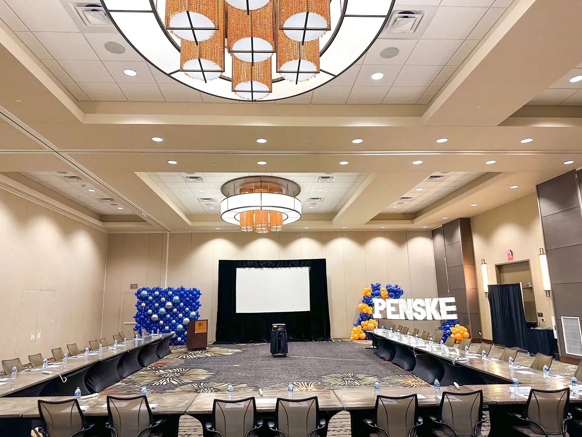 Conference room set up for a presentation. Tables in U-shape, blue and gold balloons,
