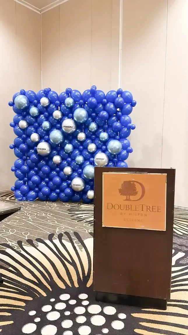 A blue balloon wall with silver accents behind a DoubleTree hotel sign on a patterned floor.
