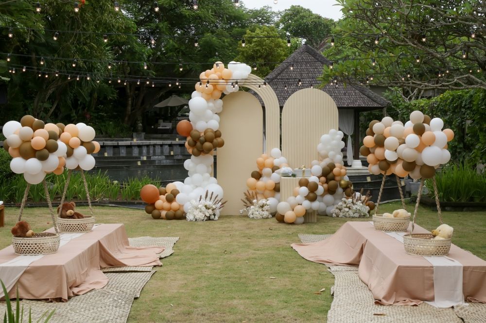 Balloon-decorated outdoor wedding setup with beige tables, lounge seating, and floral arches in a garden