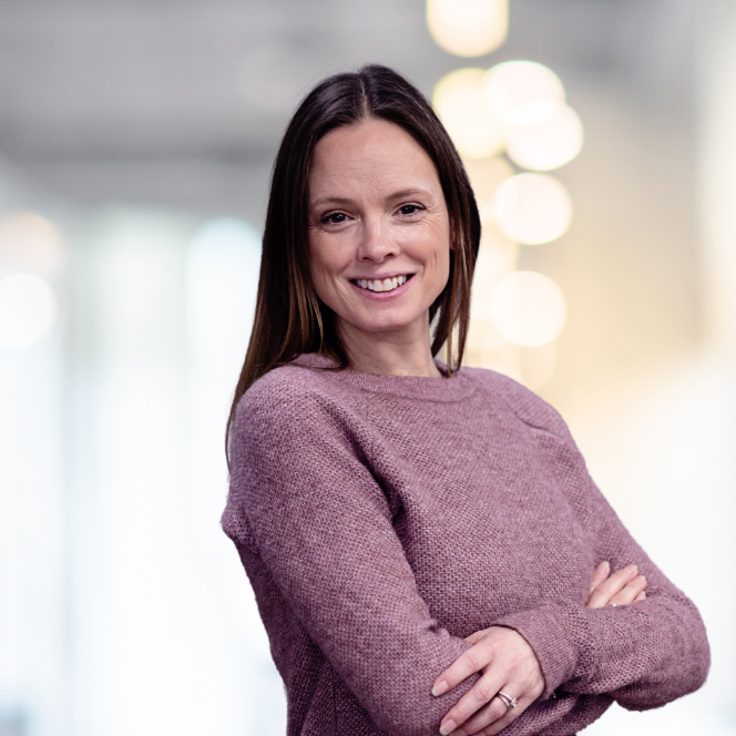 A woman is sitting on a couch talking to another woman while holding a laptop.