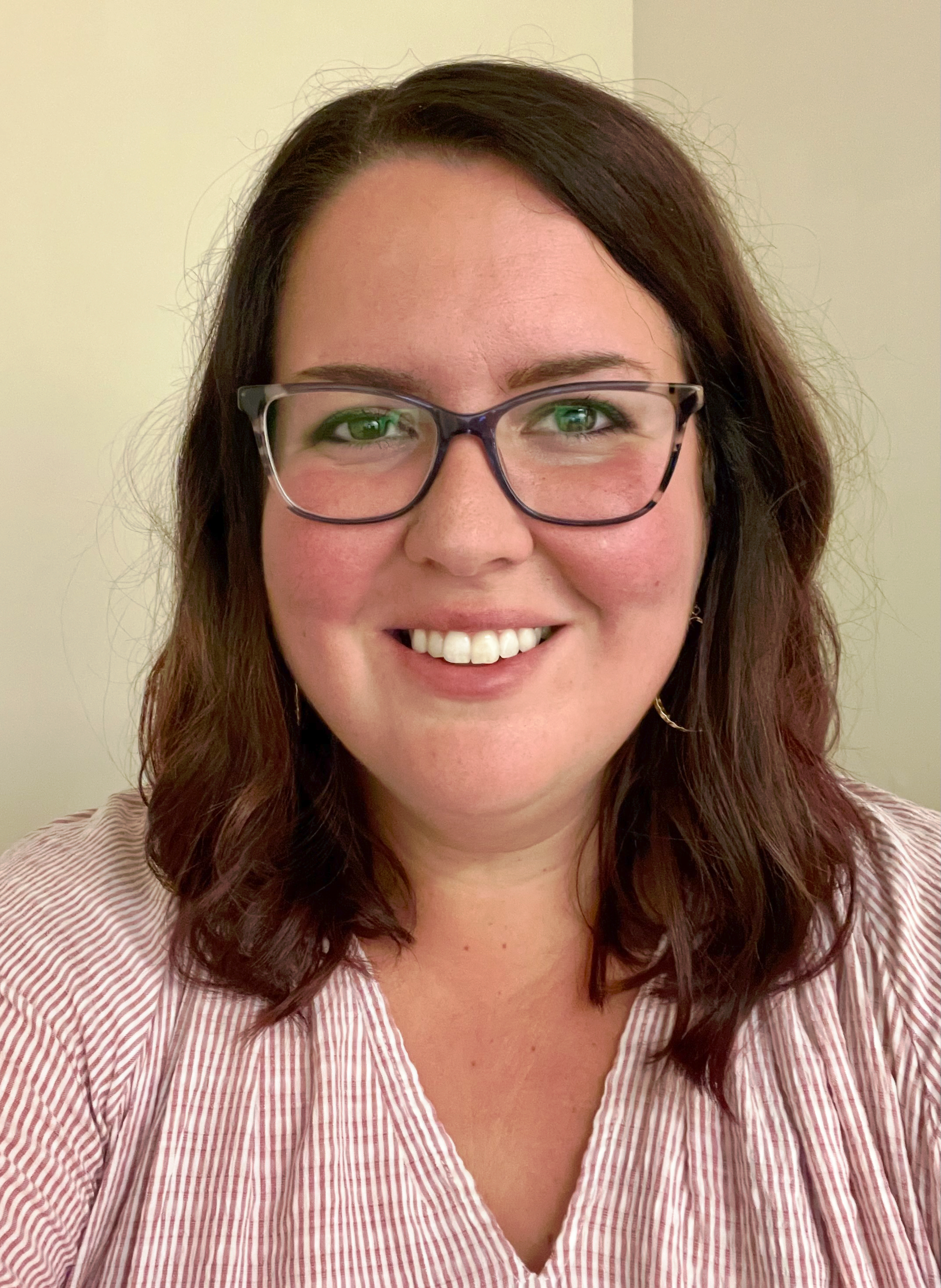 A woman is sitting on a couch talking to another woman while holding a laptop.