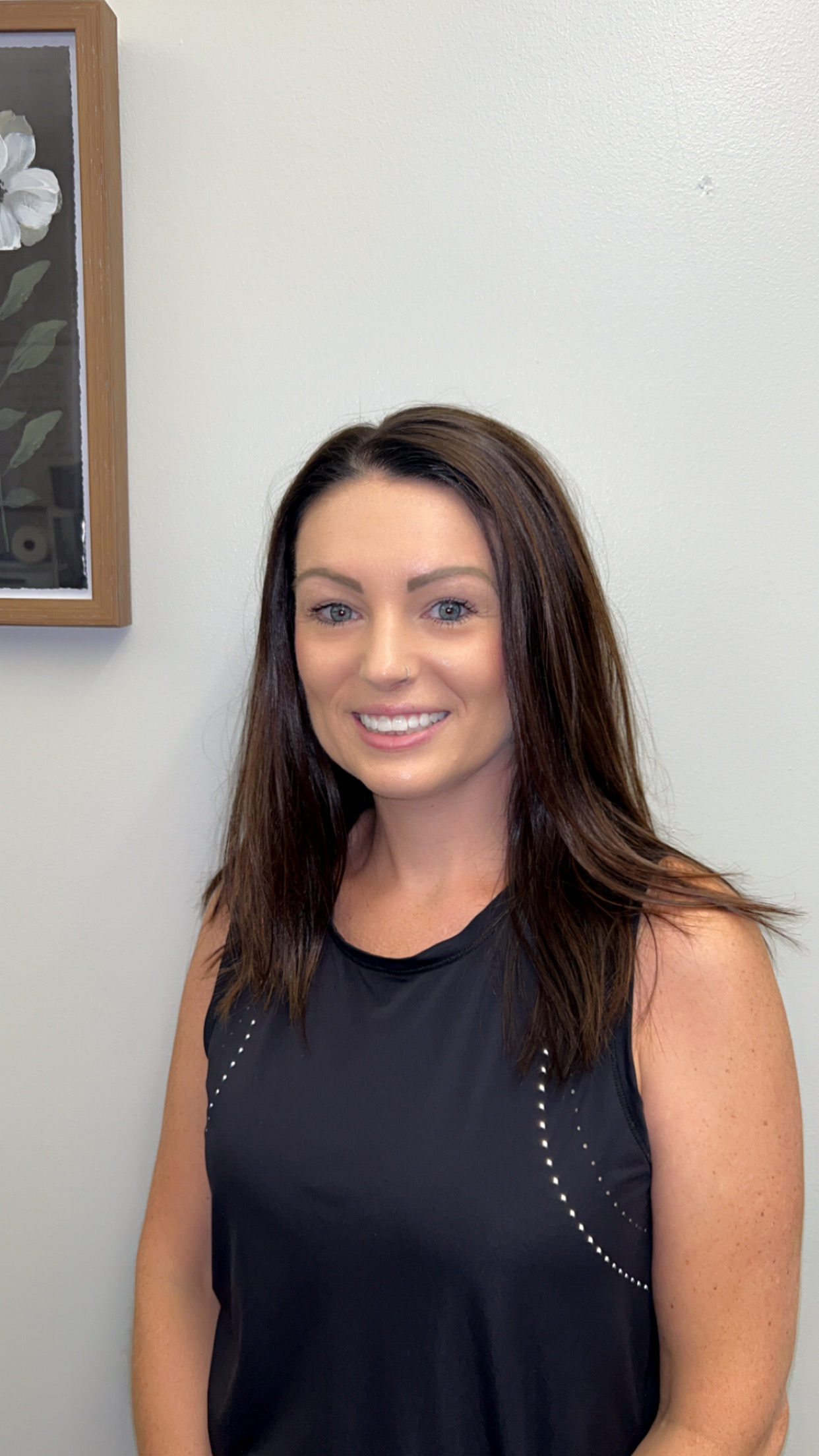 A woman is sitting on a couch talking to another woman while holding a laptop.