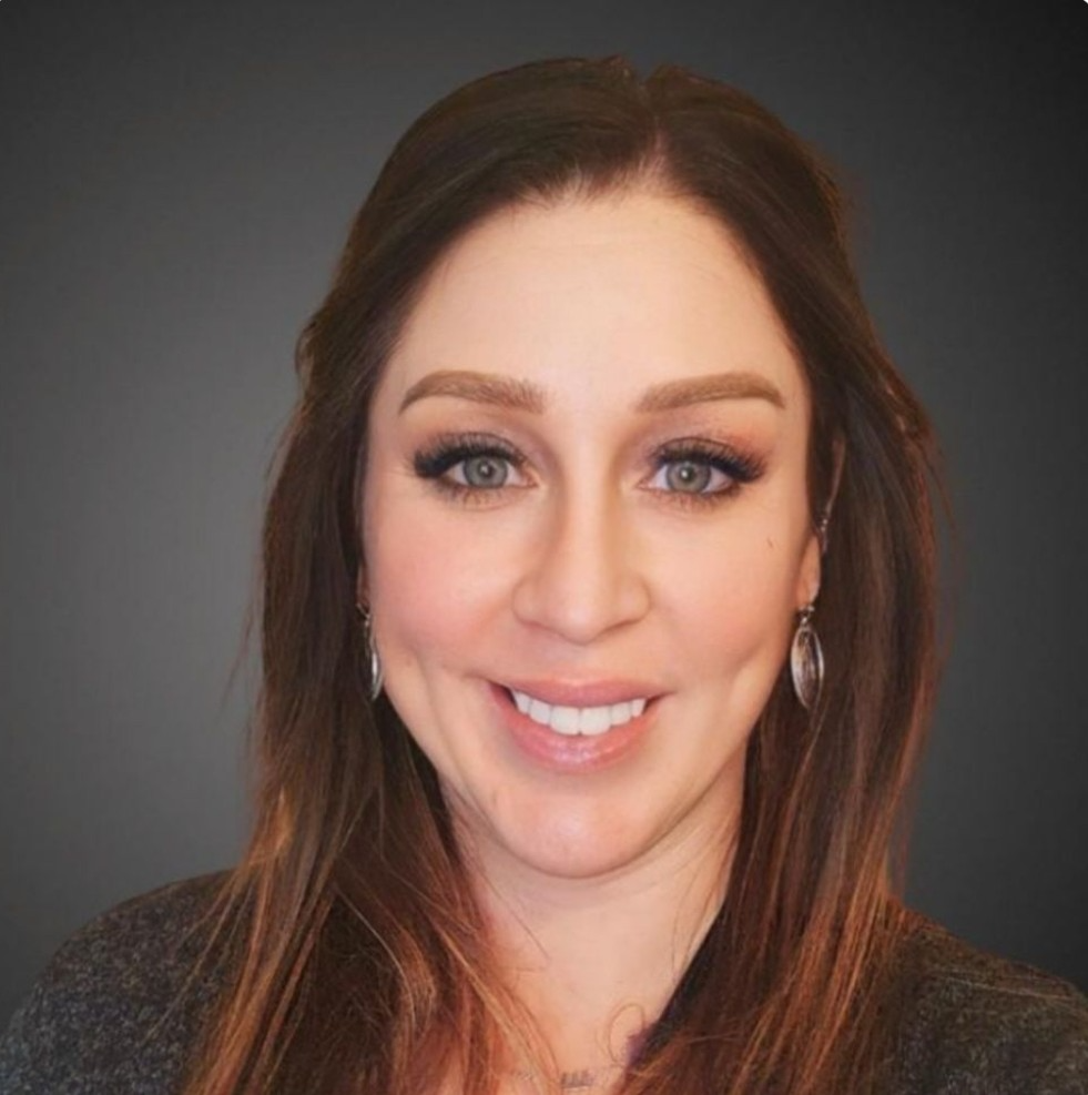 A woman is sitting on a couch talking to another woman while holding a laptop.