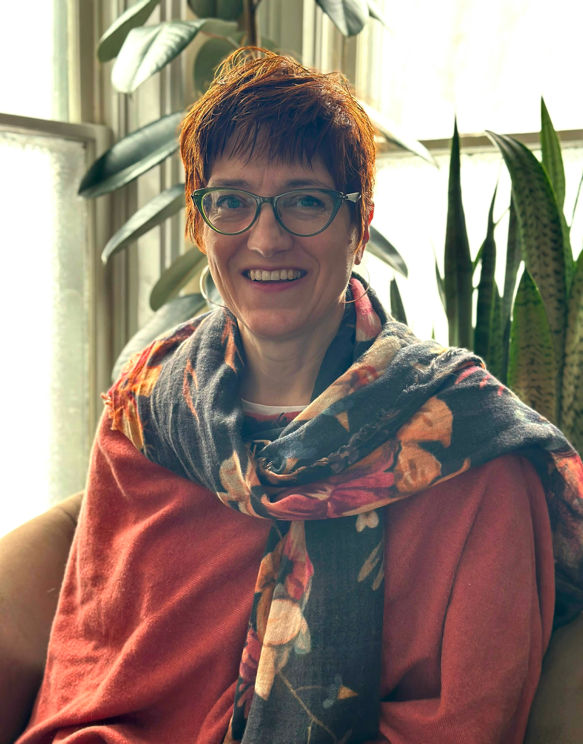 A woman is sitting on a couch talking to another woman while holding a laptop.