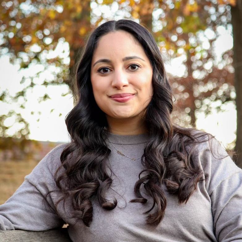 A woman is writing on a clipboard while a man wearing a mask looks on.