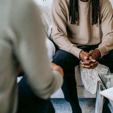 A man is sitting on a couch talking to another man.