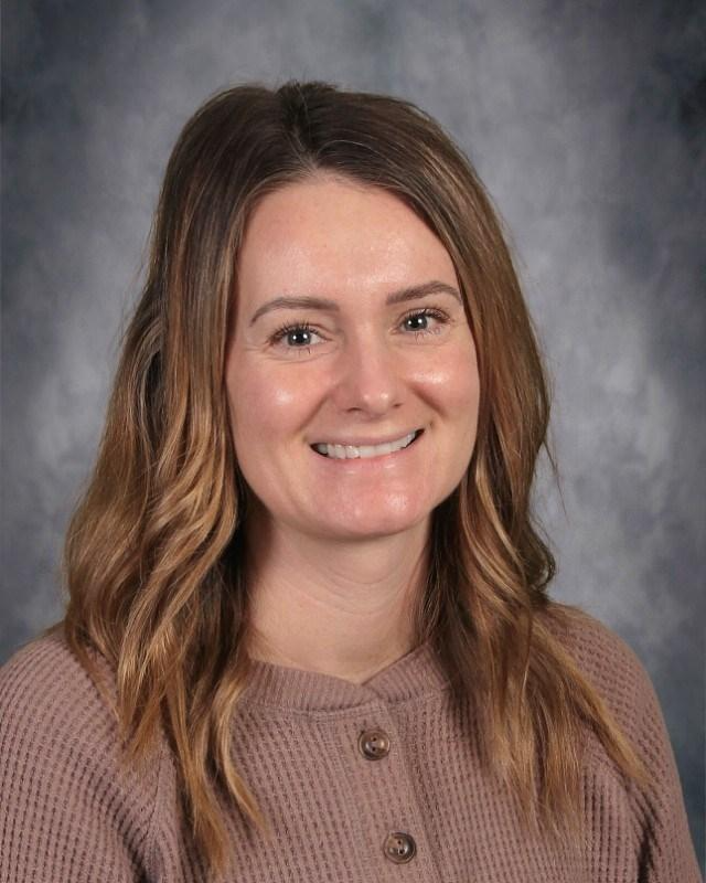 A woman is sitting on a couch talking to another woman while holding a laptop.