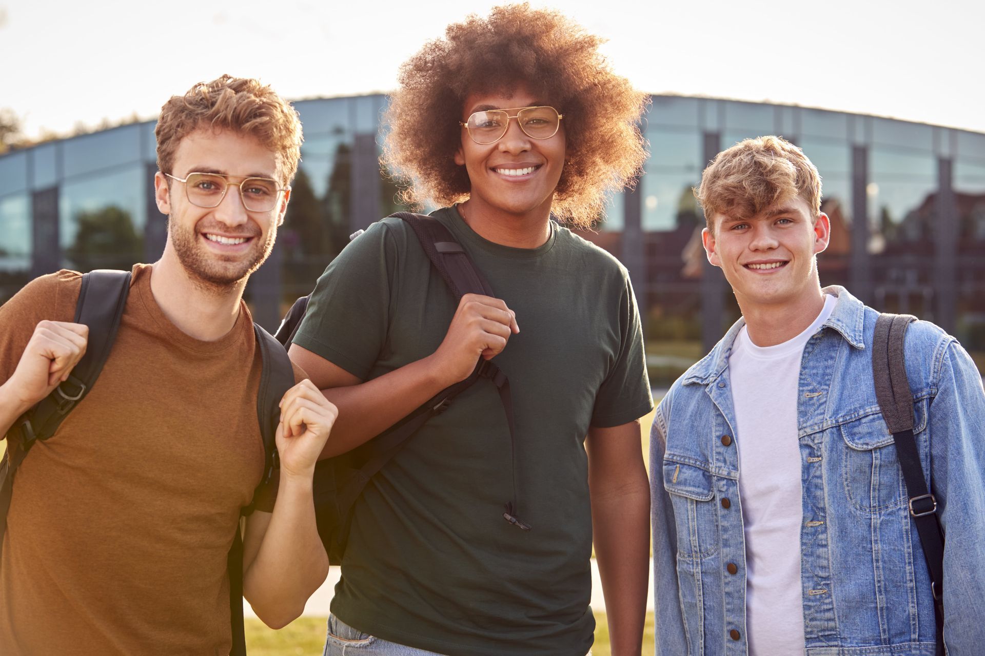 Three young men with backpacks are standing next to each other in front of a building.