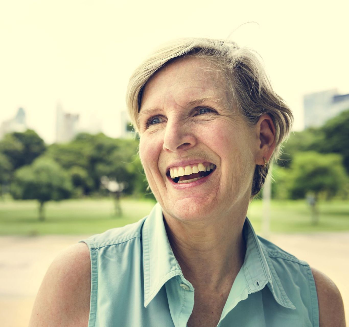 A woman in a blue shirt is smiling in a park.