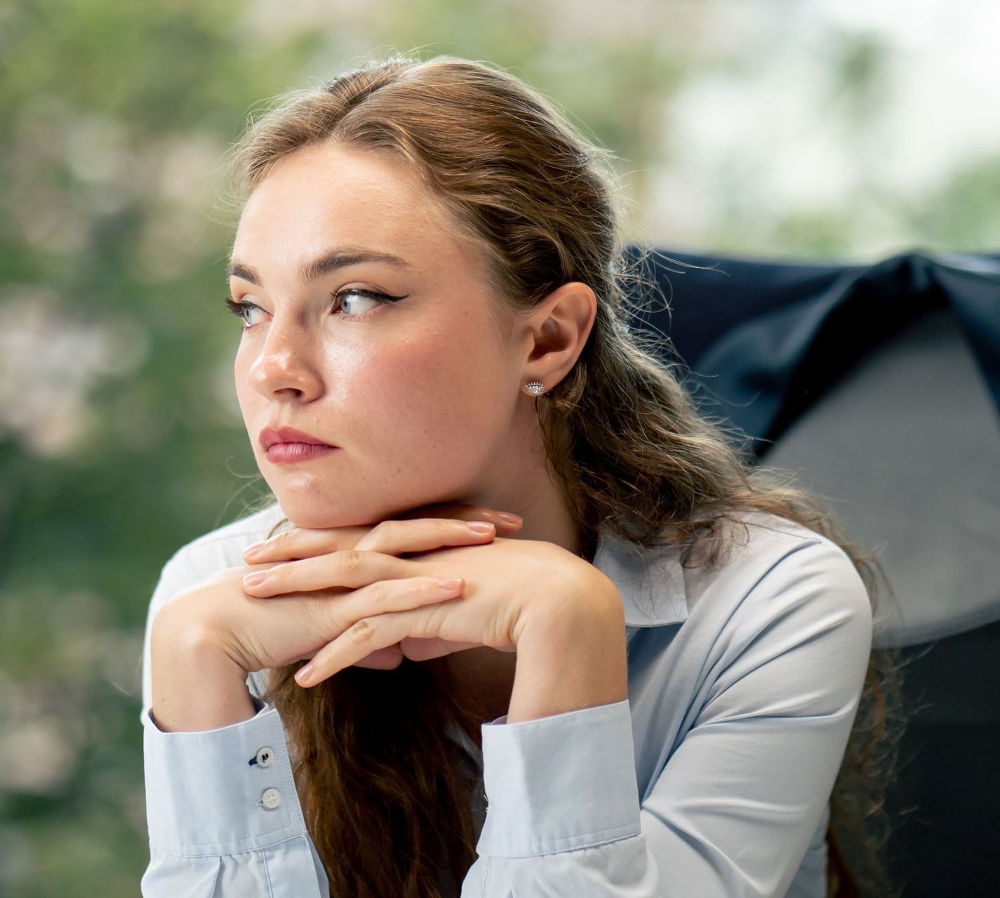 A woman is sitting in a chair with her hands on her chin.