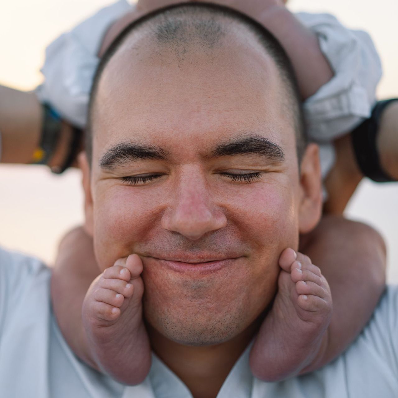 A man is smiling while holding a baby on his shoulders