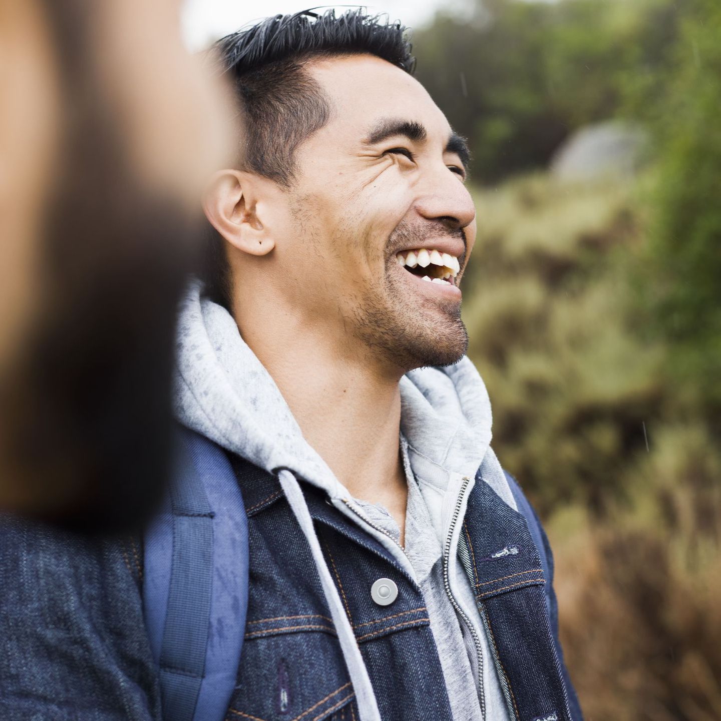 A man wearing a denim jacket and a backpack is smiling