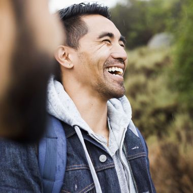 A man wearing a denim jacket and a backpack is smiling