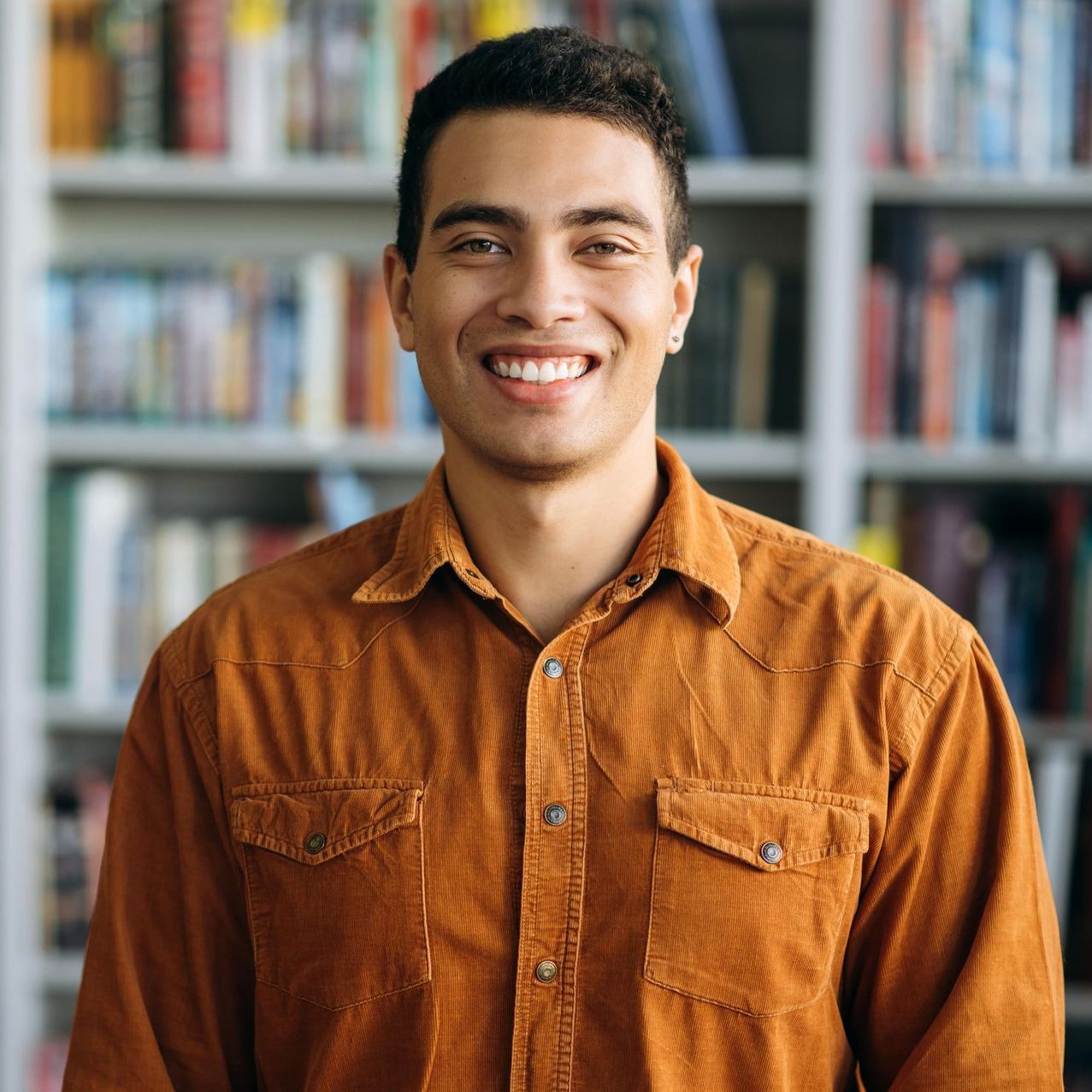 A man is walking down a sidewalk while holding a book and looking at his phone.