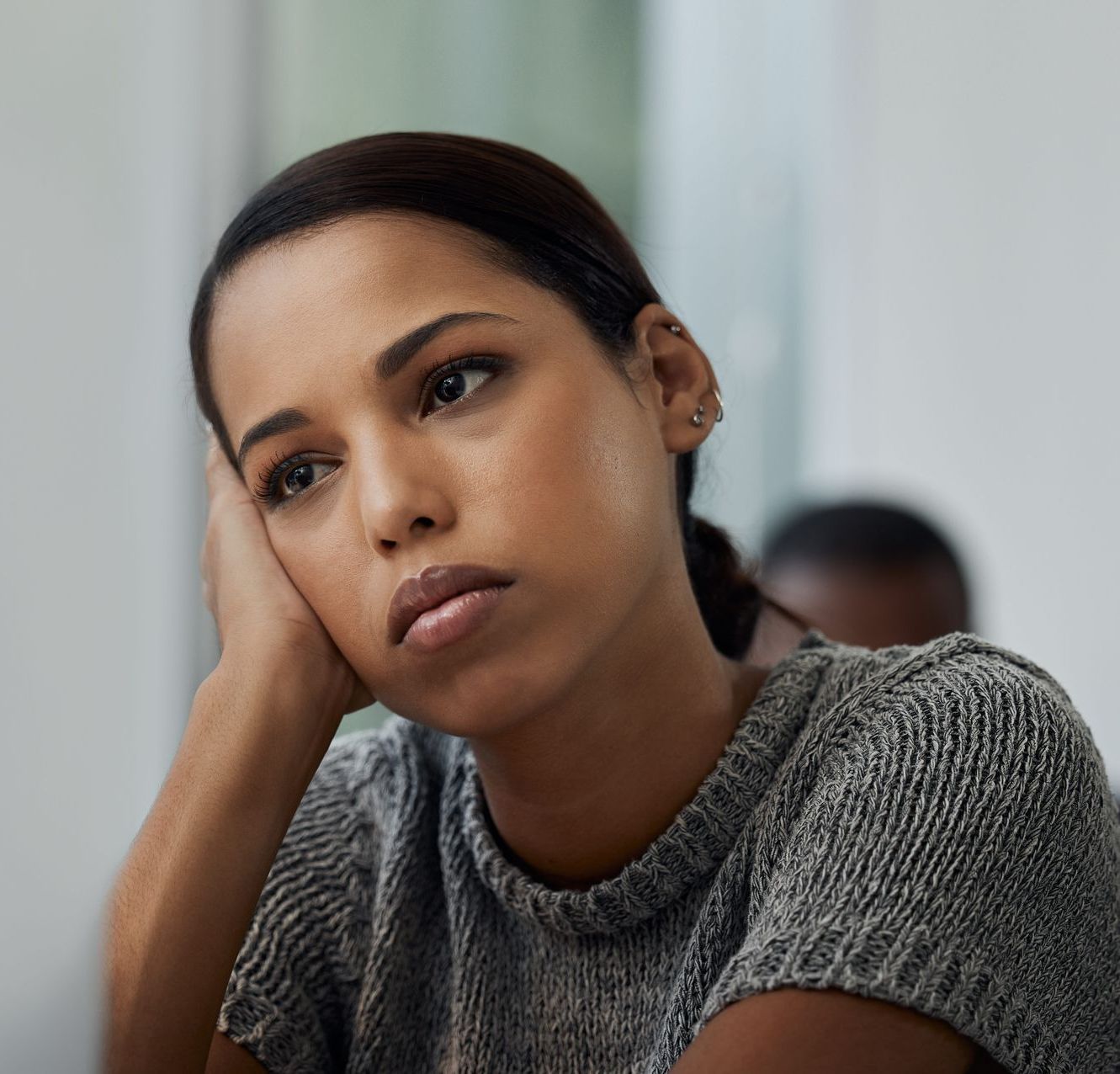 A woman in a grey sweater rests her head on her hand