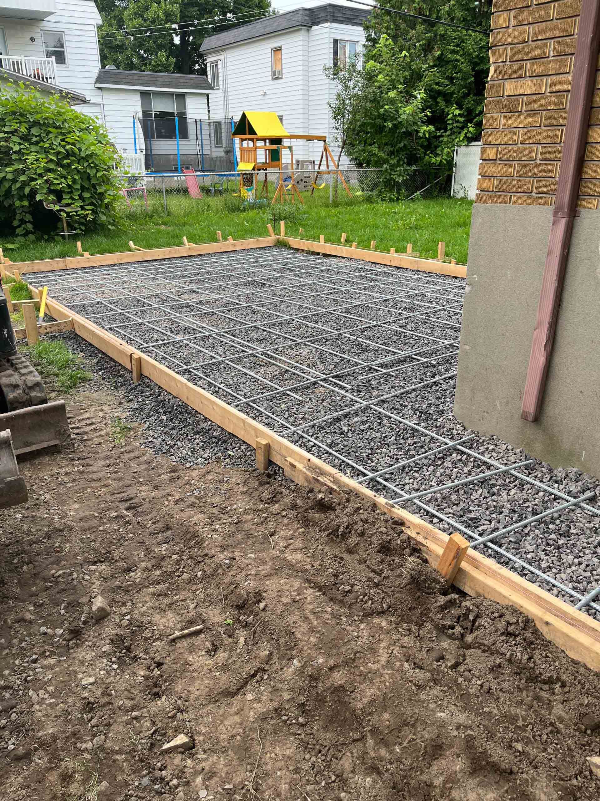 Parterre de jardin rempli de gravier, bordé de bois, à côté d'un carré de terre et d'une maison dans une cour arrière.