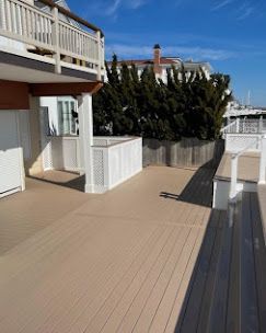 A large wooden deck with a white railing and a bench.