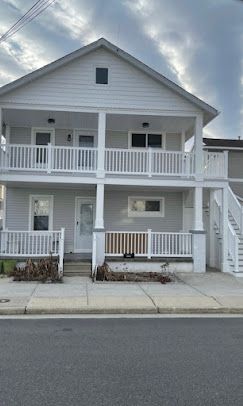 A large white house with a porch and stairs is sitting on the side of the road.