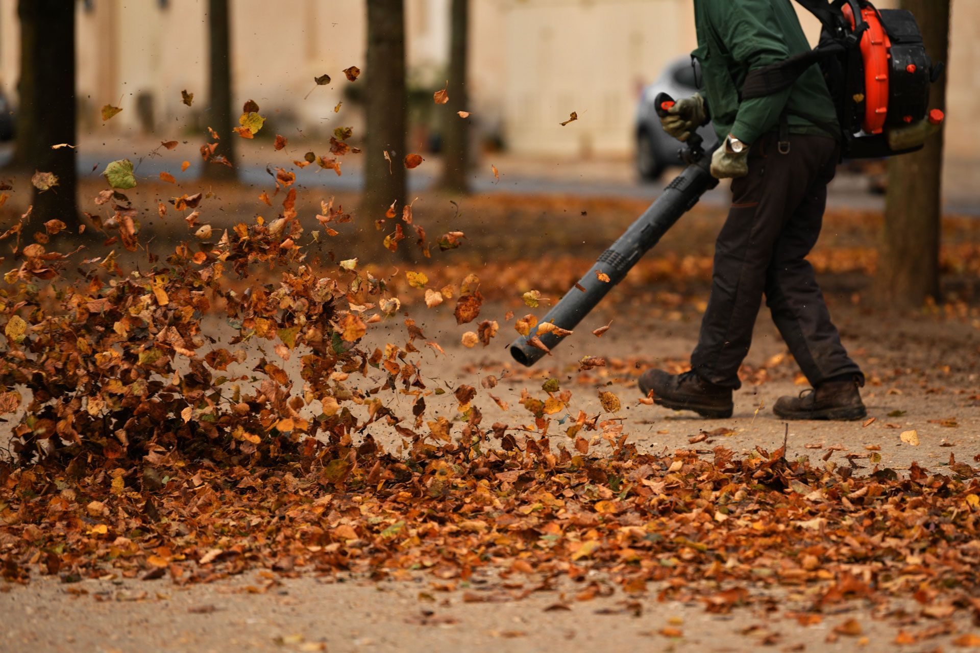 A man is blowing leaves on the sidewalk with a leaf blower.