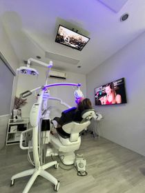 Person in a dentist chair undergoing a procedure, illuminated with purple light, watching TV.