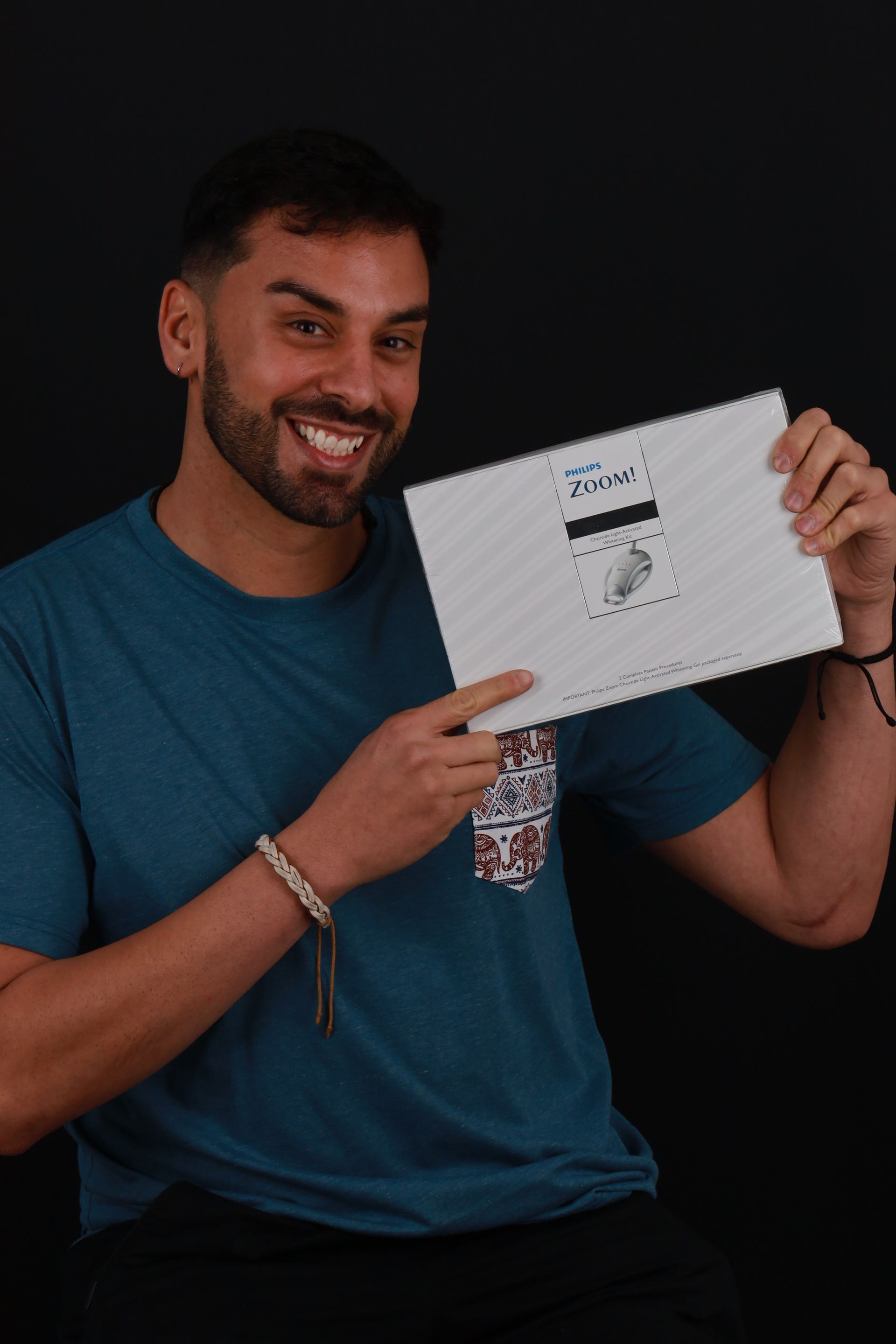 Man smiling, holding a white paper with a printed design, against a black background.