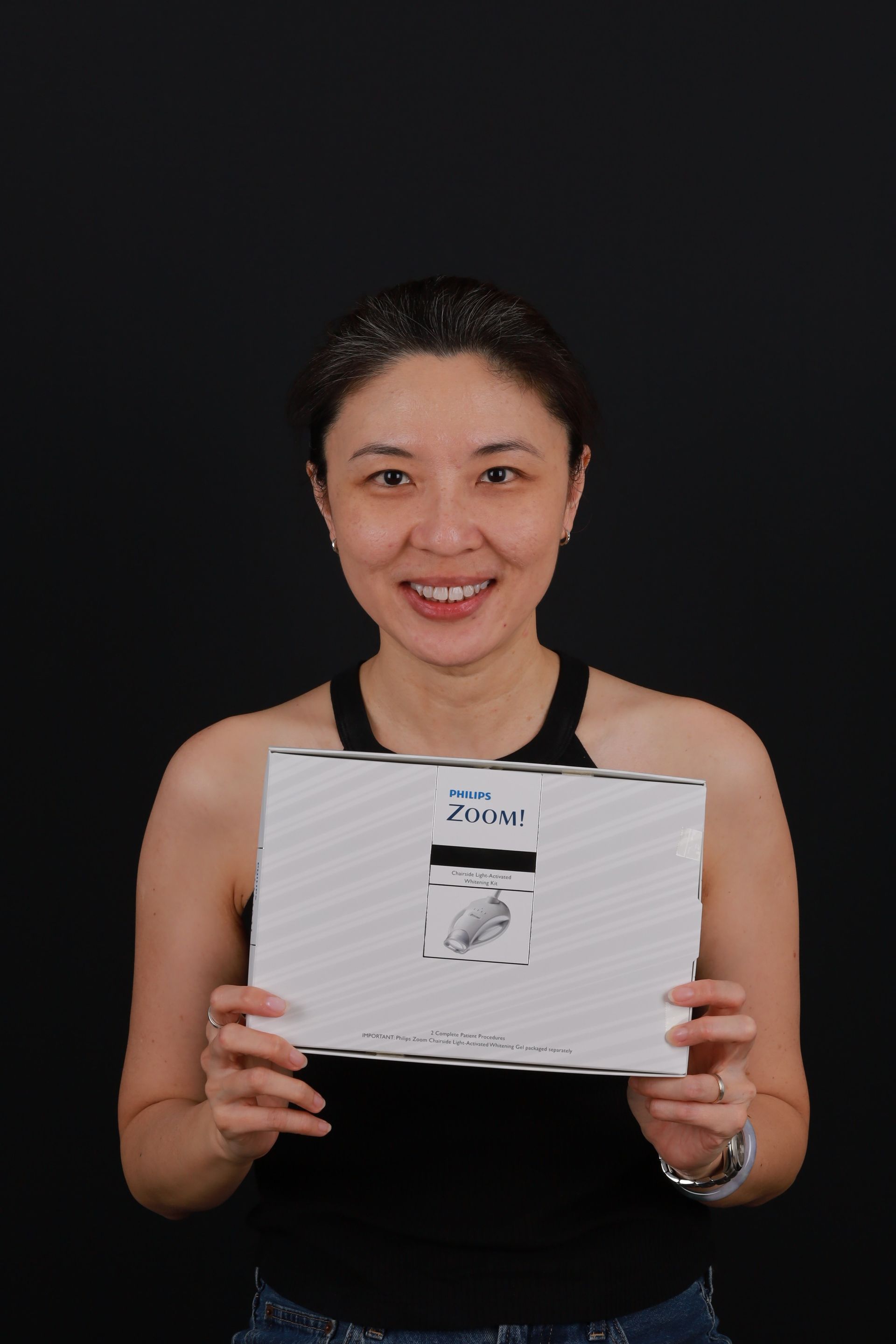 Woman smiling, holding a white box with text and image of a device, black background.