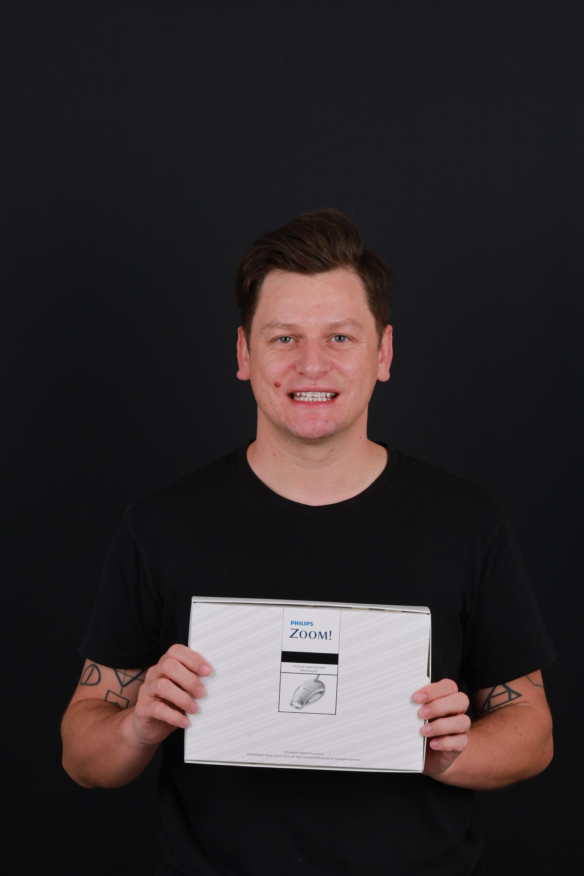 Man holding a paper with image in front of black background. Man wearing black shirt smiles.