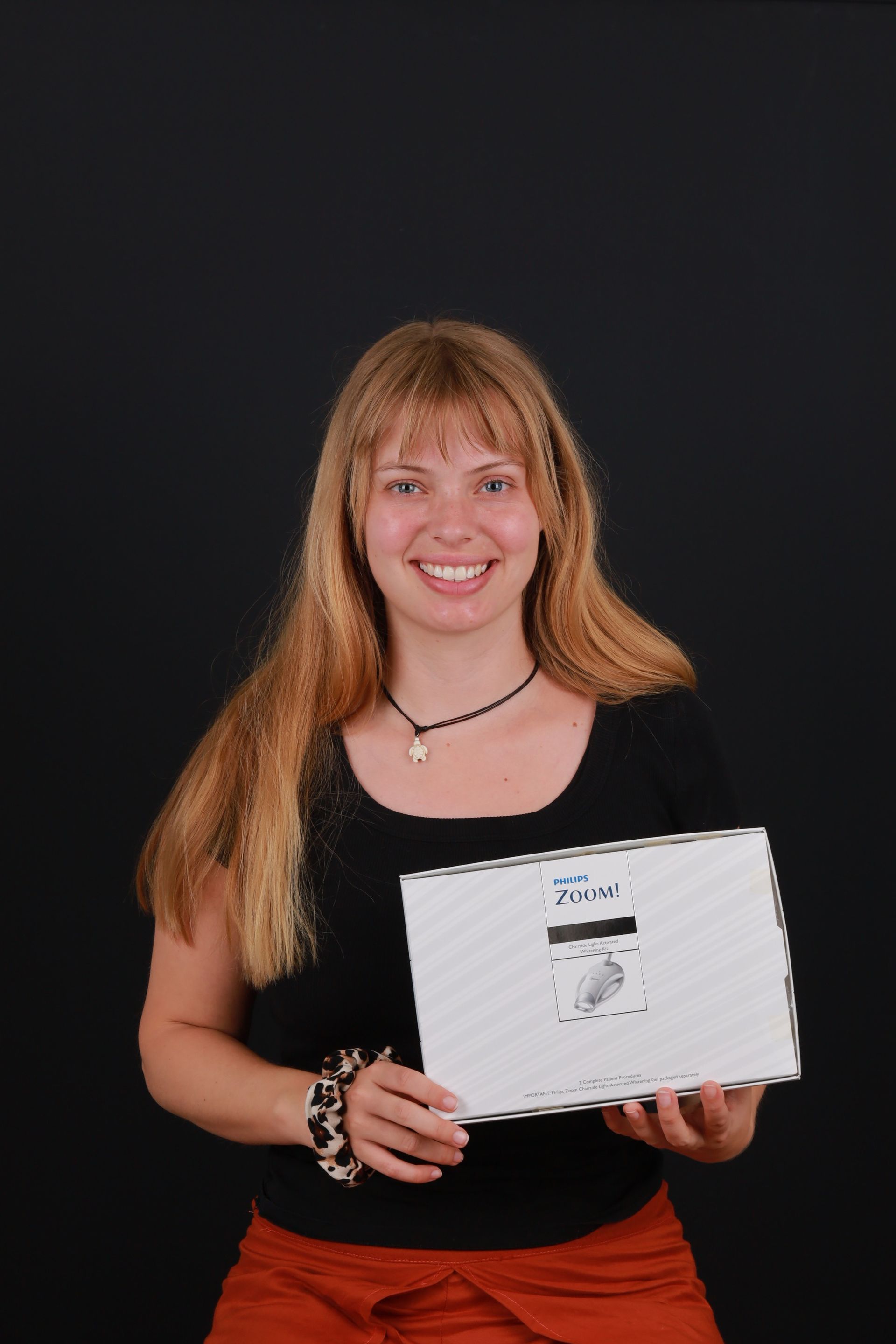 Blonde woman smiles, holds white box with black background.