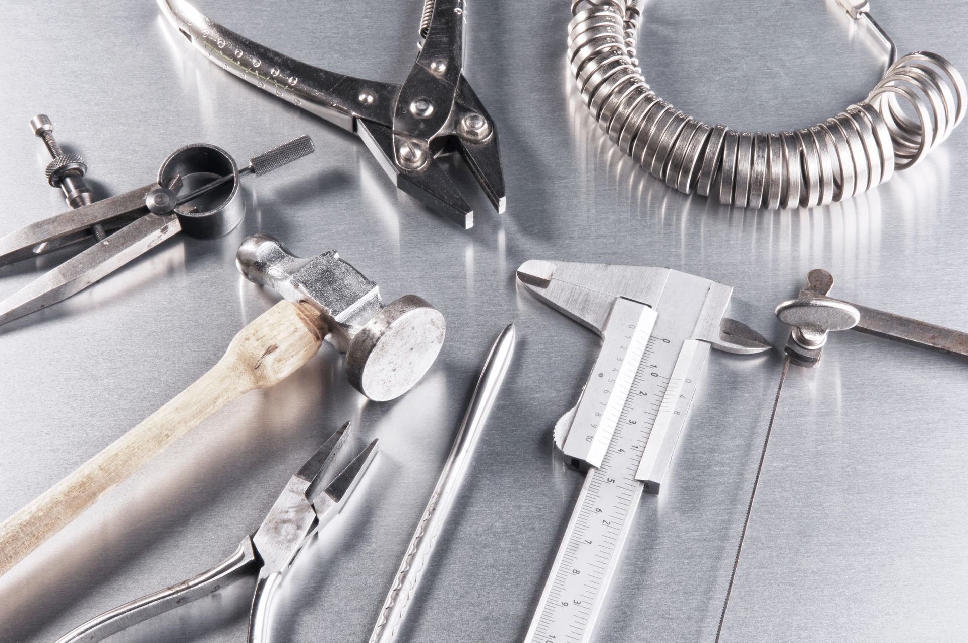 Strumenti per la creazione di gioielli su una superficie metallica lucida: pinze, martelli, misuratori per anelli, calibri.