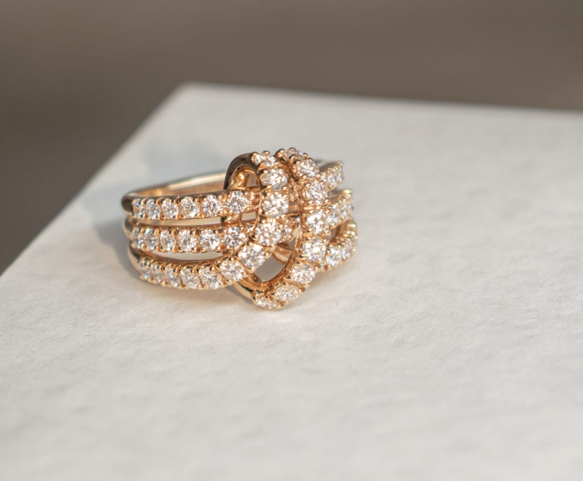 Anello in oro con diamanti, caratterizzato da un motivo a nodo con tre fasce e un nodo centrale ricoperto di diamanti.