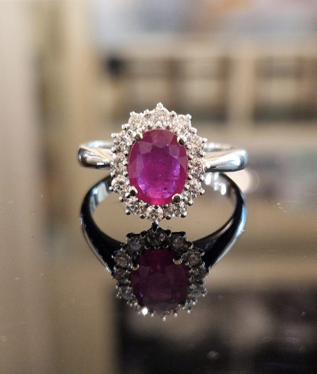 Anello ovale con rubino e diamanti che si riflettono su una superficie lucida.