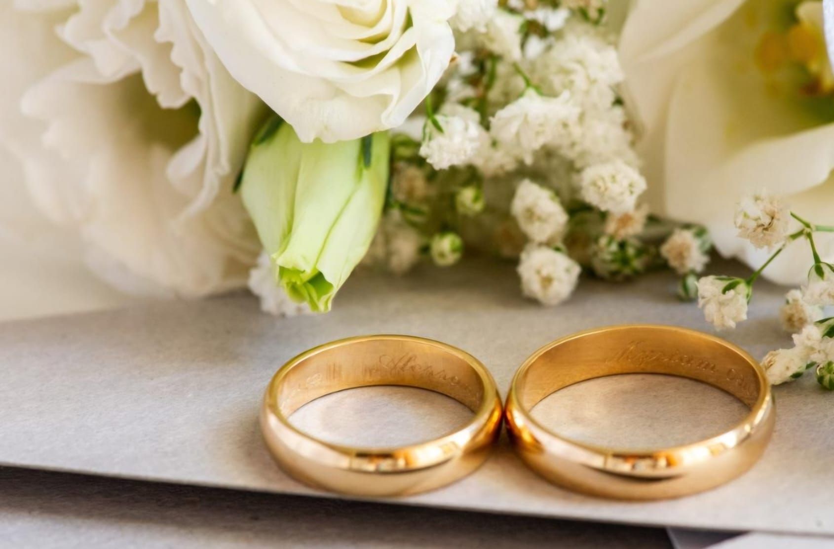 Due fedi nuziali d'oro accanto a un bouquet di fiori bianchi.