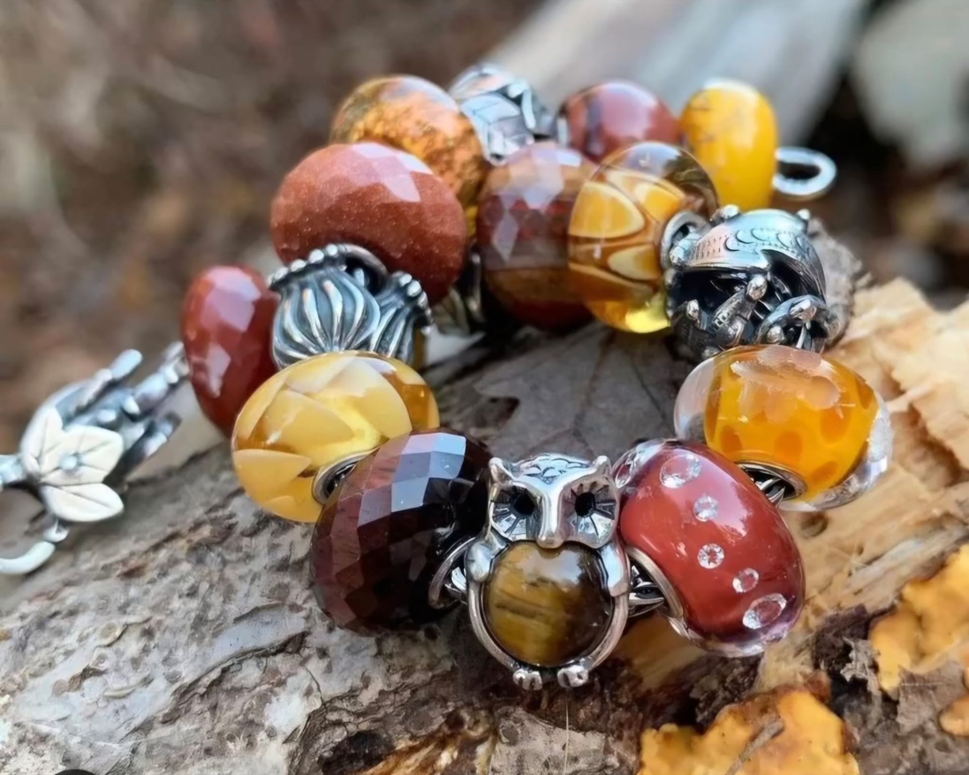 Braccialetto con varie perline marroni, arancioni e gialle, tra cui un ciondolo a forma di gufo, su una superficie di legno.