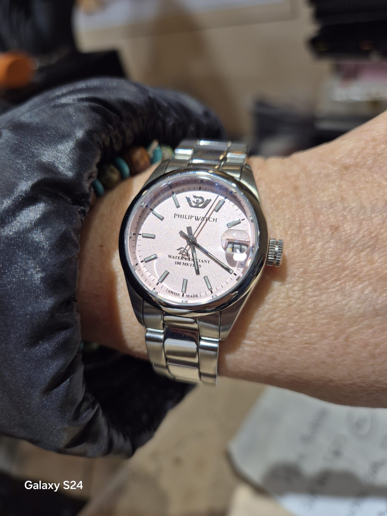 Orologio da polso con quadrante rosa chiaro, cinturino argentato, indossato con guanto nero.