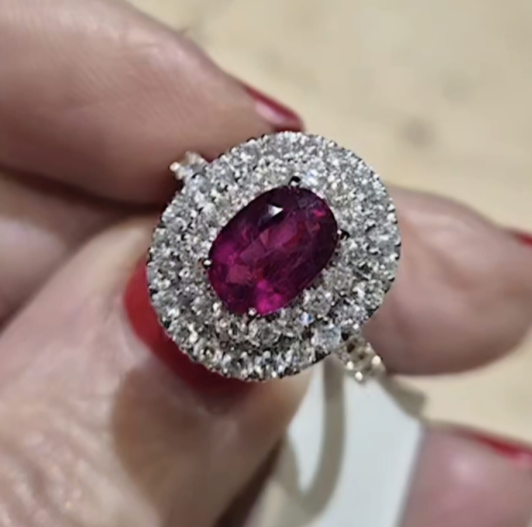 Anello ovale con rubino e diamanti, tenuto da una persona con smalto rosso.