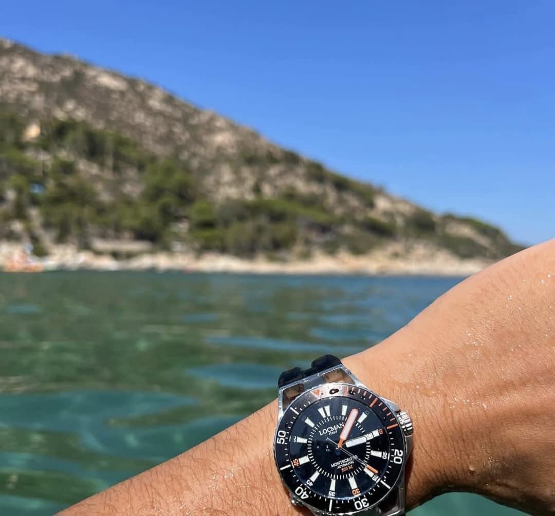 Orologio da polso con orologio subacqueo nero su sfondo di oceano, montagna e cielo azzurro.
