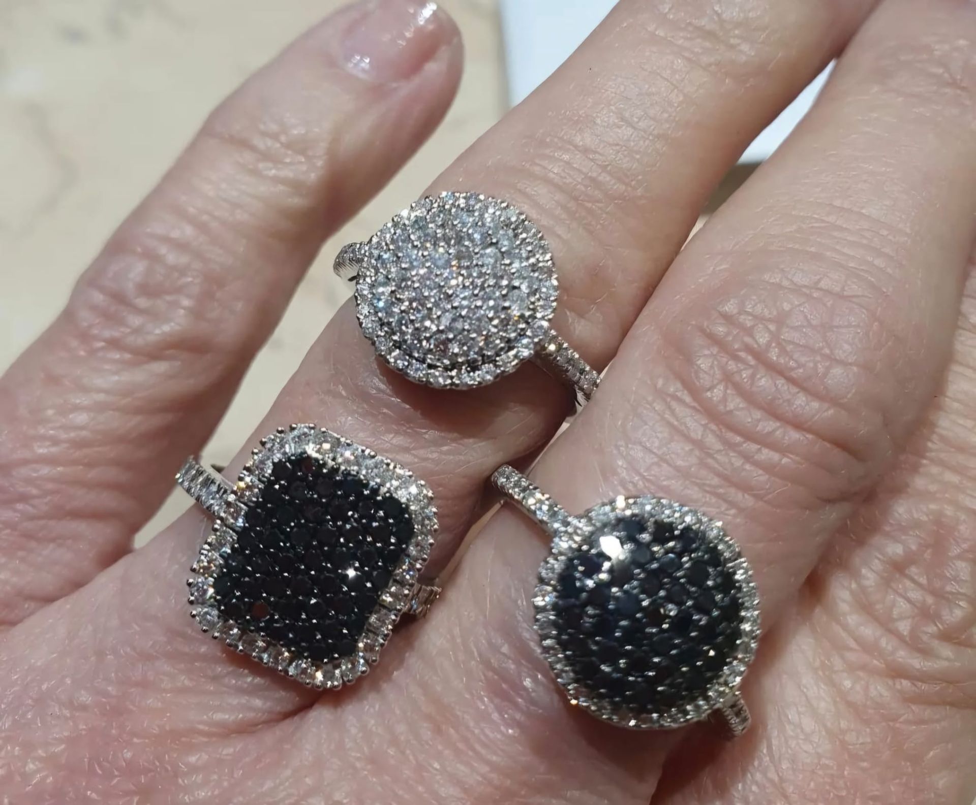 Tre anelli con pietre preziose su una mano. Un anello con pietre bianche, due con pietre nere.