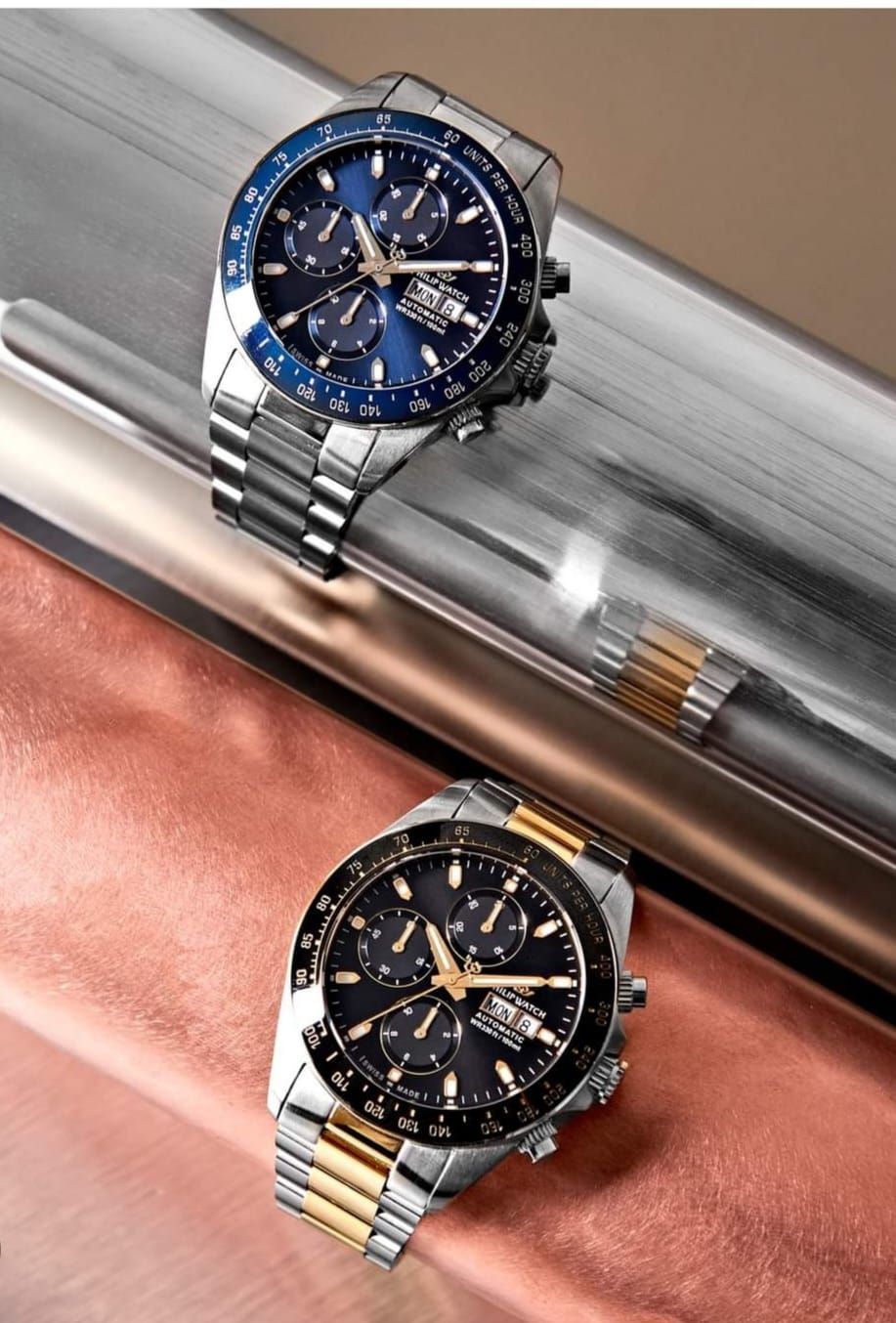 Due cronografi in acciaio inossidabile, uno con lunetta blu, l'altro con lunetta dorata, su superfici riflettenti.
