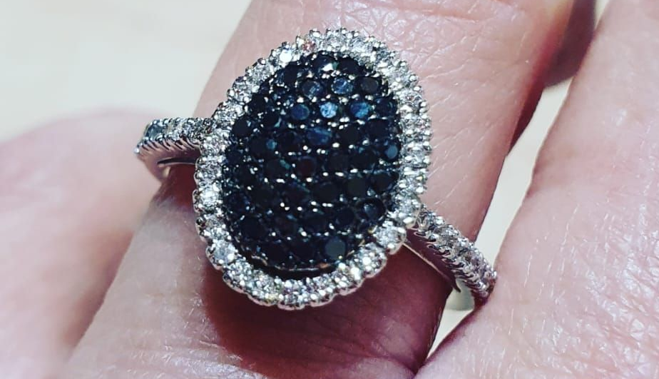 Primo piano di un anello d'argento con una gemma nera ovale circondata da gemme bianche, indossato al dito.