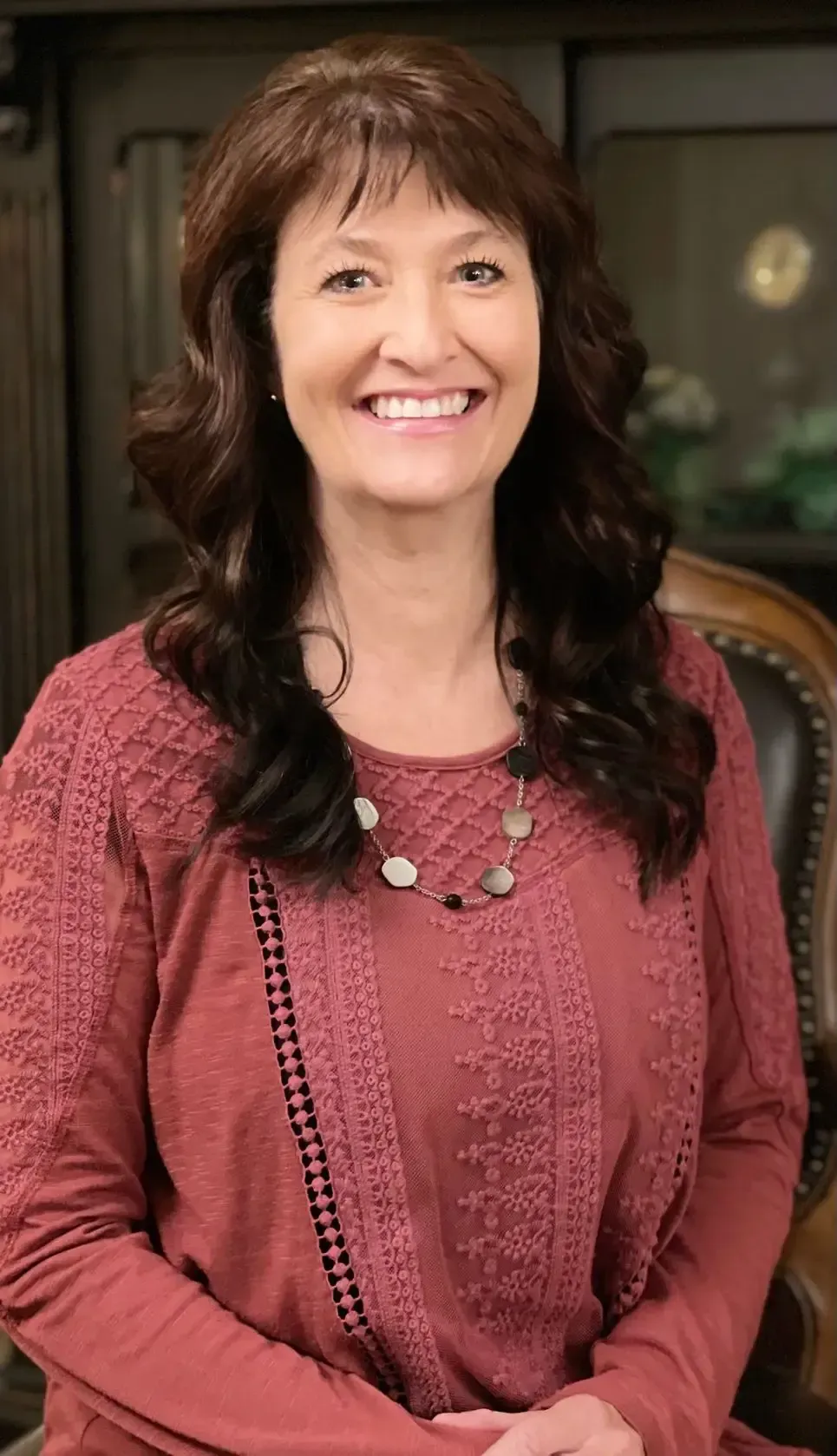 a woman wearing a red shirt and a necklace smiles for the camera