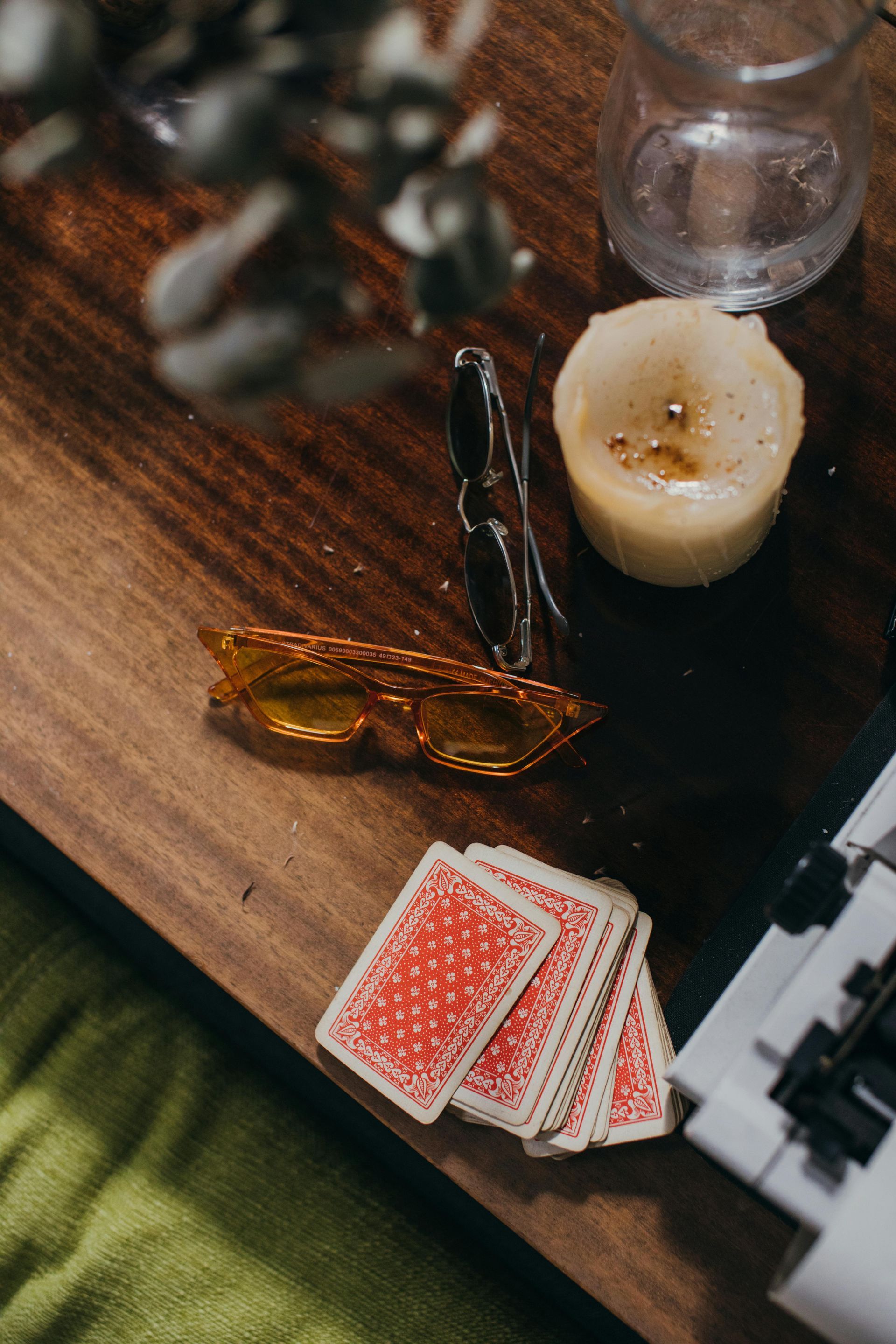 Sunglasses, playing cards, and lit candle on a wooden table.